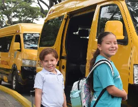 Two smiling students with backpacks stand beside a yellow school bus, ready to board for school transportation.